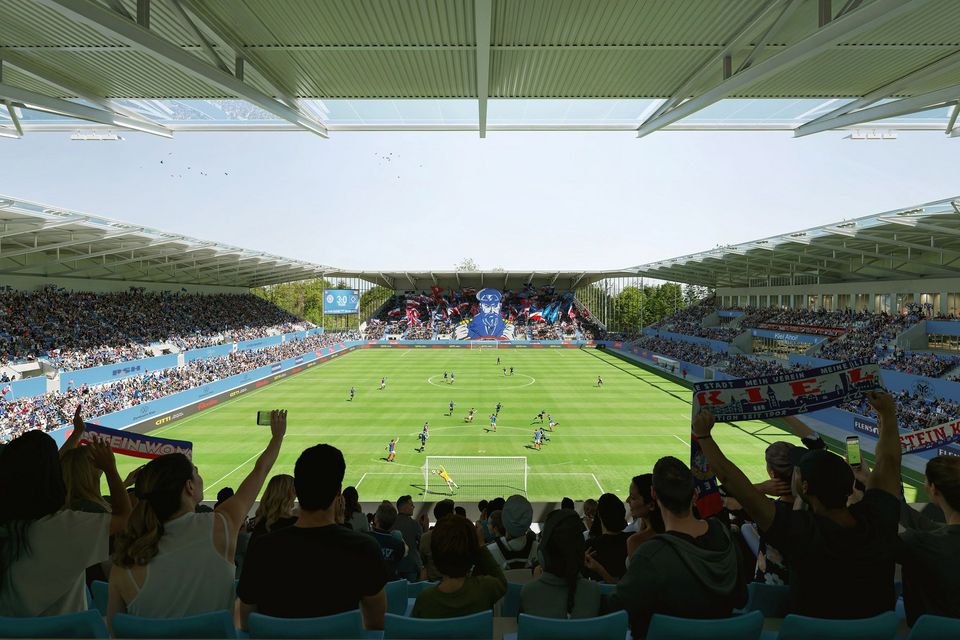 Interior view of a modern football stadium from the stands, showing the pitch, full spectator tiers and an active match scene.