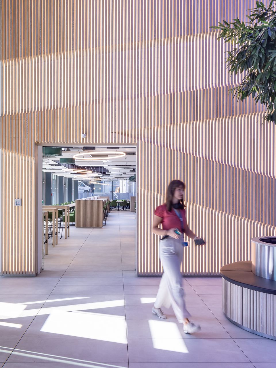 Interior view of a foyer featuring a full‑height slatted wall, a central passage and a view into an open work and lounge area.