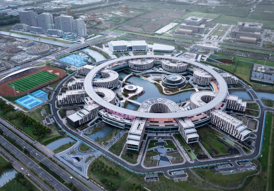 Aerial view of a large-scale research and education campus featuring a circular central building, surrounding water landscapes, landscaped outdoor areas and adjacent sports facilities.