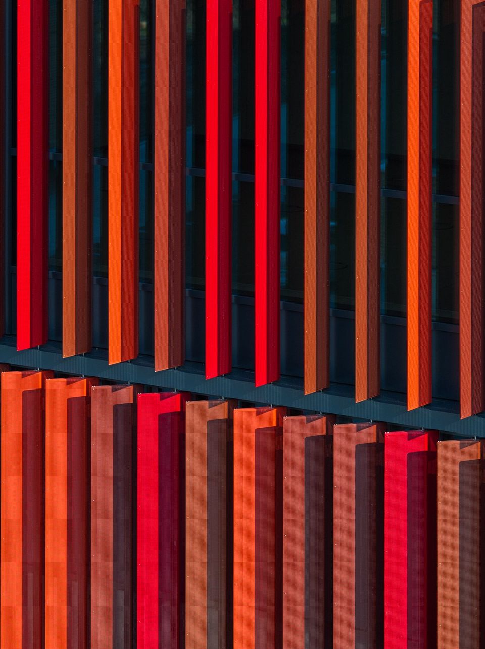Close-up of a modern façade with vertically arranged slats in varying shades of red.
