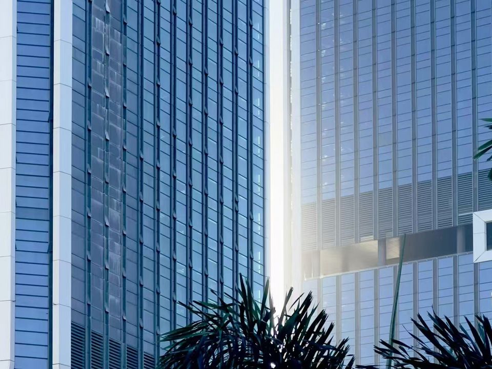 Nahaufnahme einer modernen Hochhausfassade mit vertikalen Glas- und Metallstrukturen, aufgenommen aus bodennaher Perspektive im urbanen Umfeld.