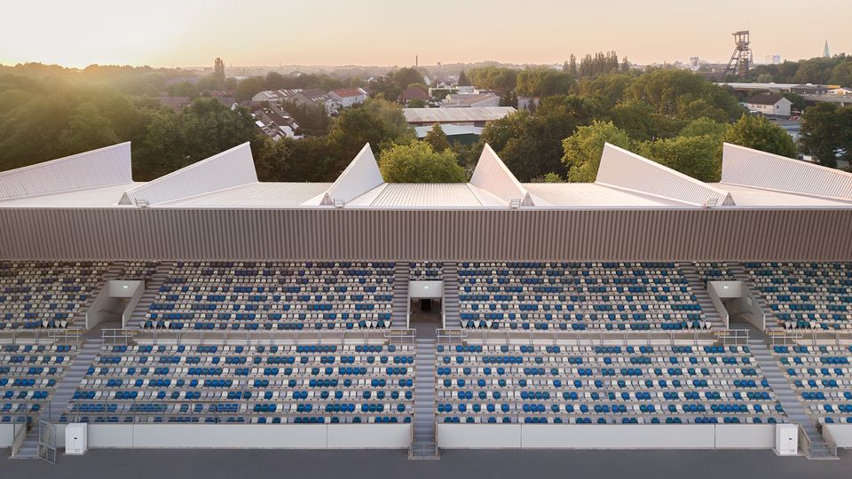 Außenvisualisierung eines Stadions bei tiefem Sonnenstand mit beleuchteter Spielfläche, überdachter Tribüne und umliegenden Grünflächen.