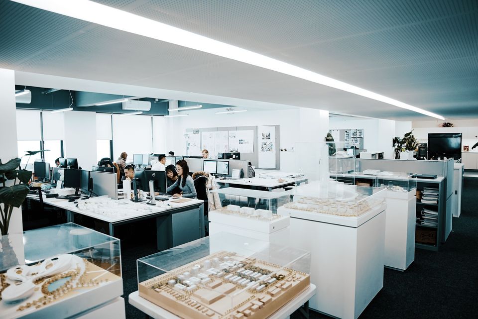 Interior view of an open-plan office with multiple workstations, computer setups, drawing desks and an organised project environment.