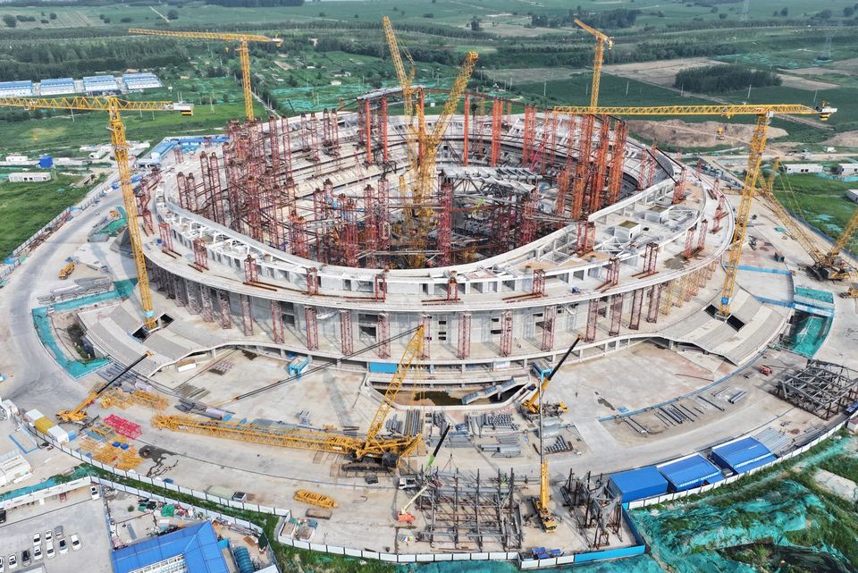 Aerial view of the arena construction site with erected structural columns, extensive site area and crane equipment.
