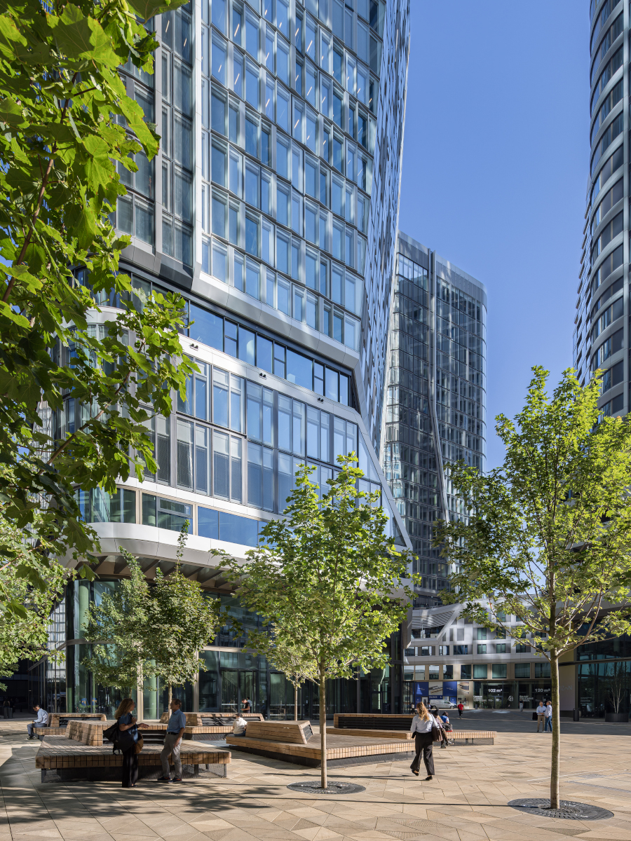 Street‑level view of a high‑rise under construction with installed lower‑level glazing, exposed concrete floors and surrounding tower cranes.